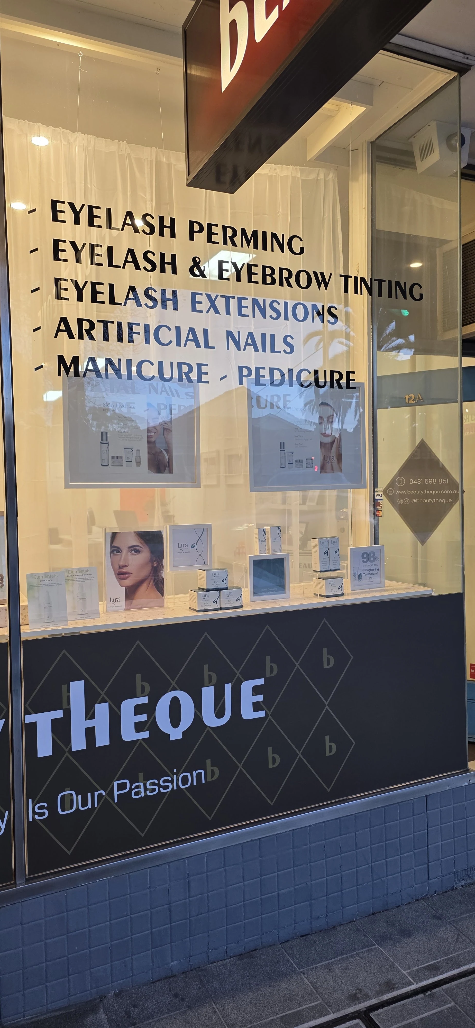 Beautytheque entry window at dusk showing the 12A gold door number, service decals, and the contact diamond reading 0431 598 851