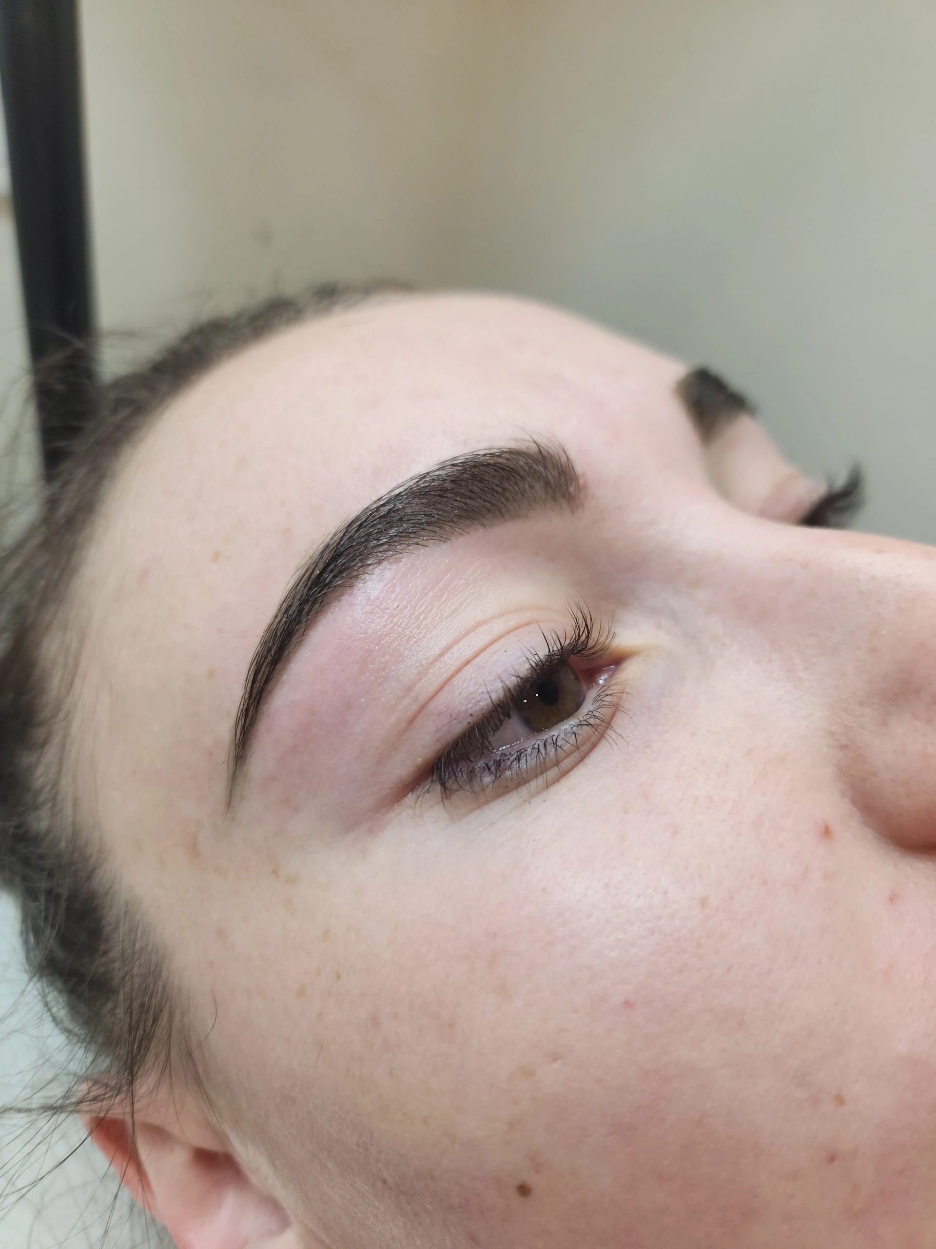 Freshly shaped and tinted brow above an open brown eye, fair freckled skin