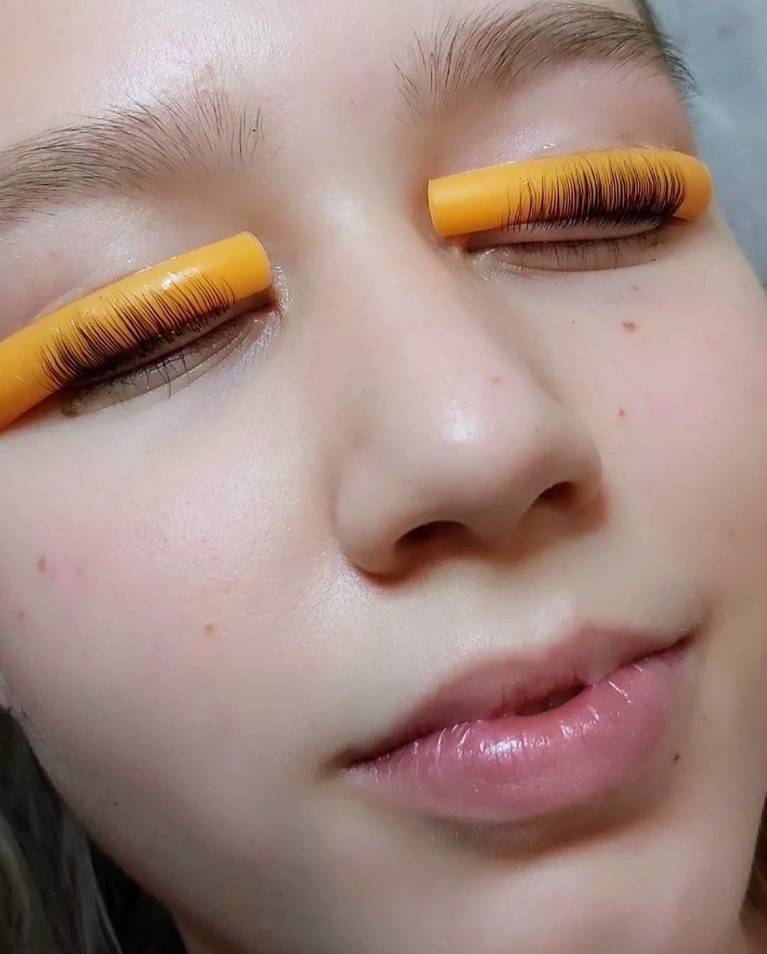 Lash lift mid-process with lashes combed onto orange silicone perming rods over closed eyes