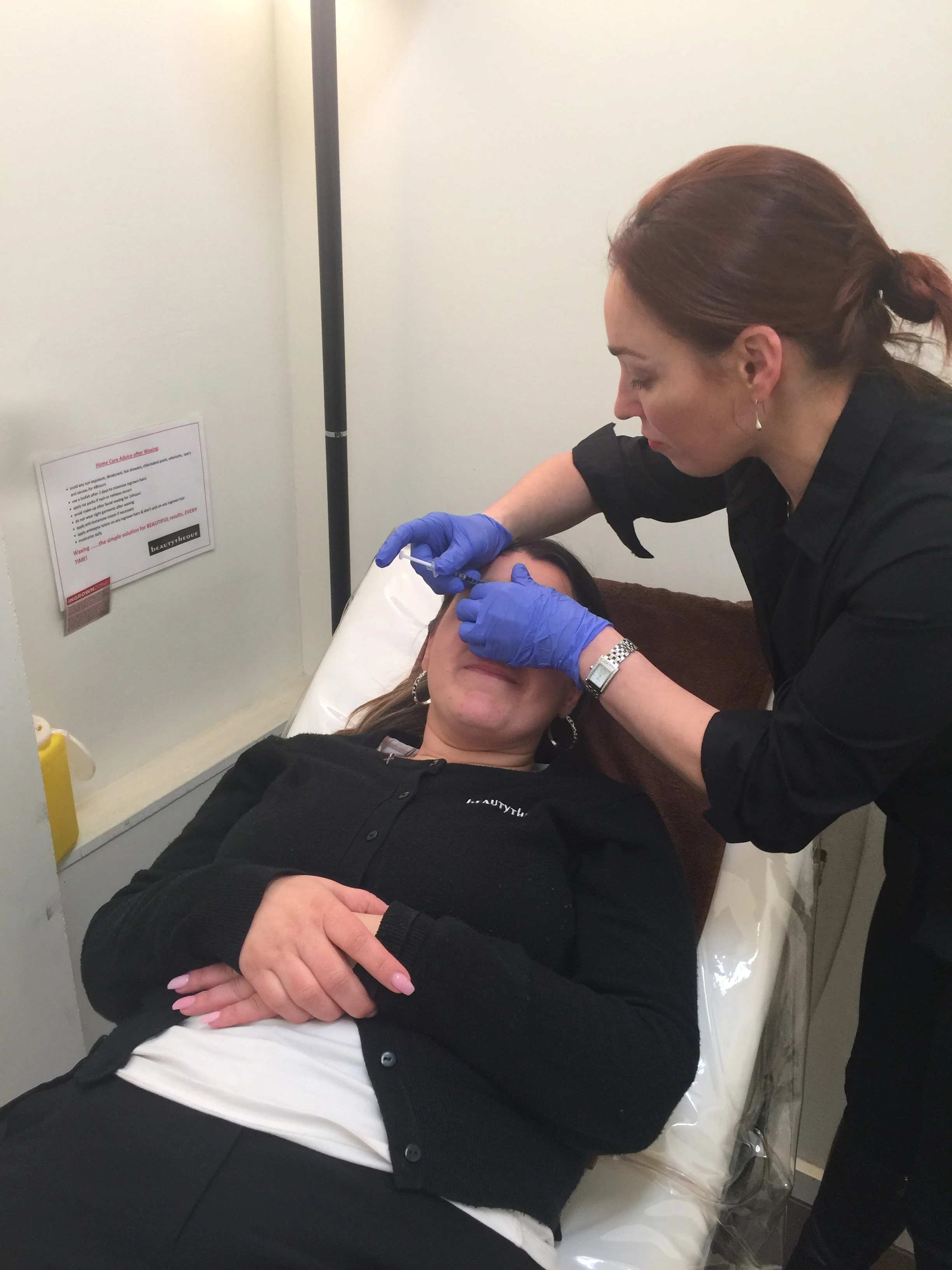 A therapist with gloved hands working on a client's brow area at the treatment station
